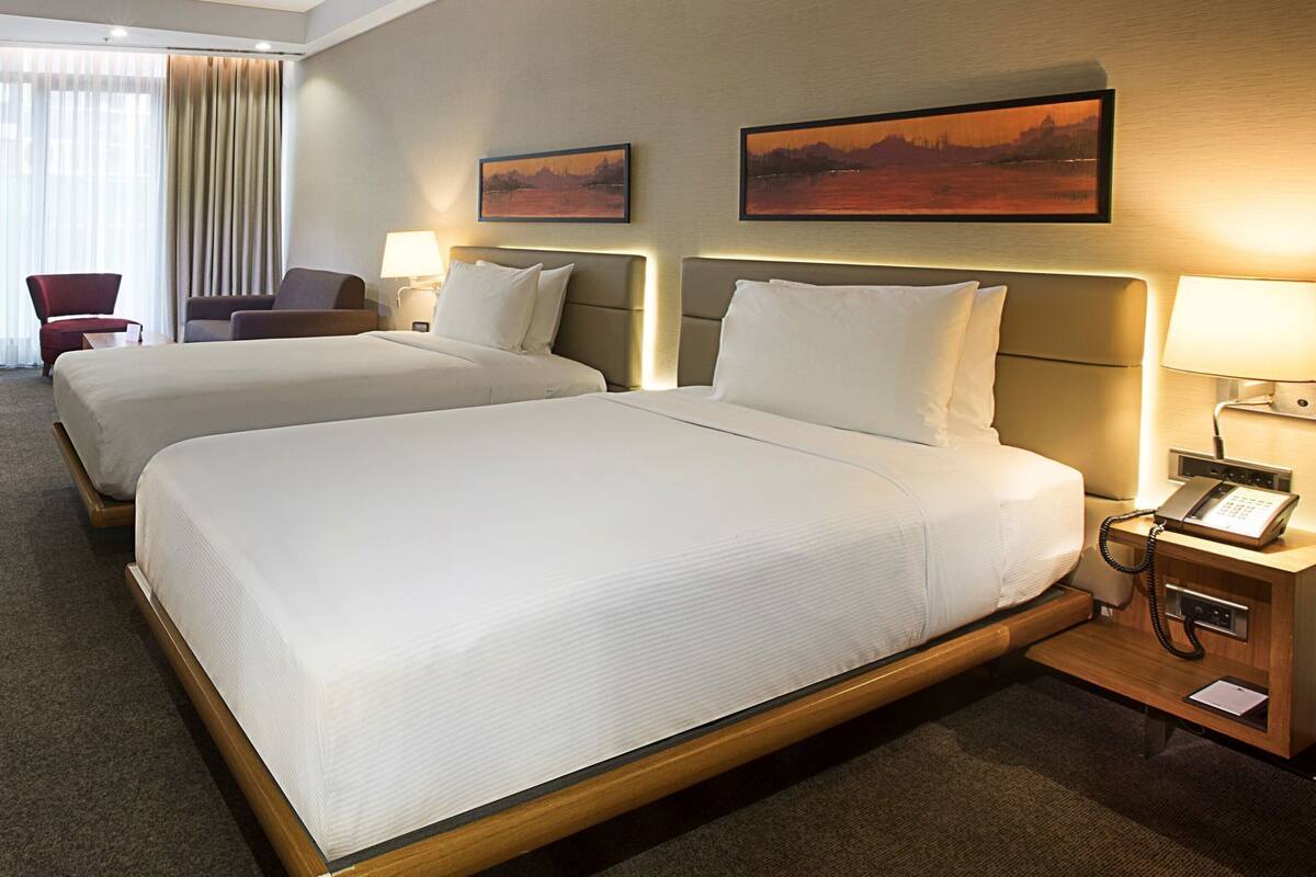 Ein Hotelzimmer mit zwei Betten, einem Schreibtisch mit Telefon und zwei Bildern an der Wand.