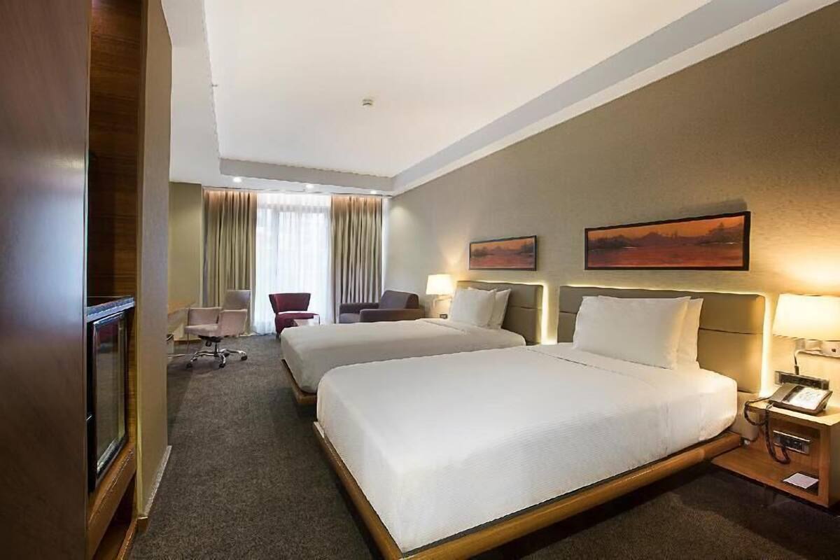 Ein Hotelzimmer mit zwei Betten, einem Schreibtisch, einem Sessel, einem Fernseher und einem Bild an der Wand.