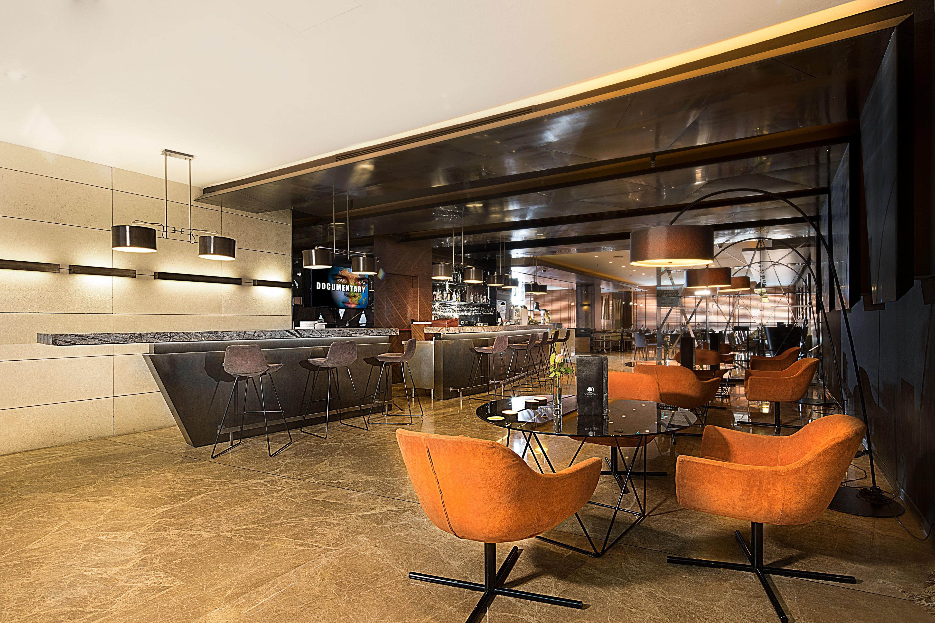 Un área de bar moderna con mostrador, asientos con taburetes y lámparas colgantes.