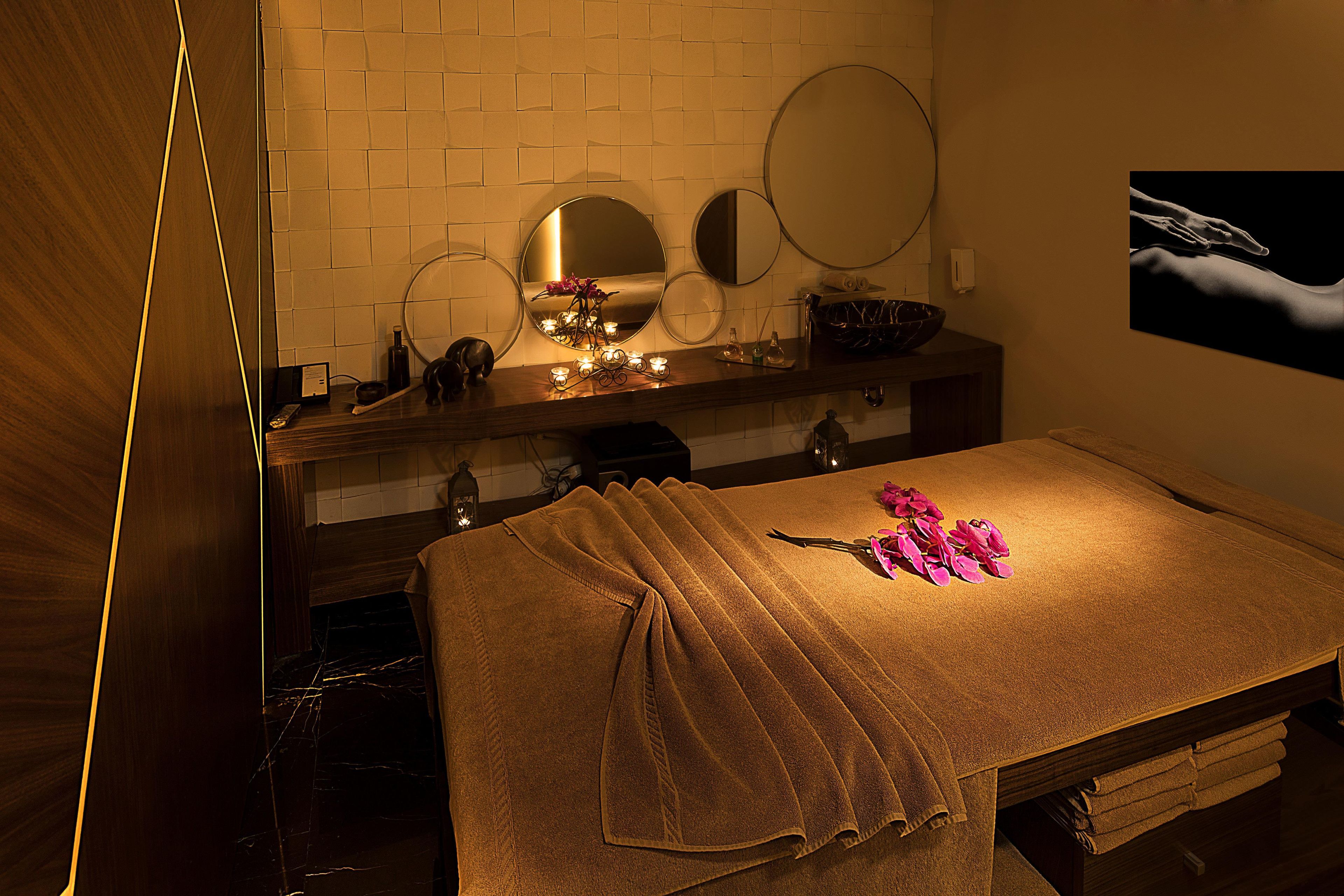 A spa room with a massage table, a mirror, a sink, and a towel rack.