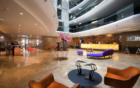 A spacious lobby with a reception desk, seating areas, and a modern chandelier.