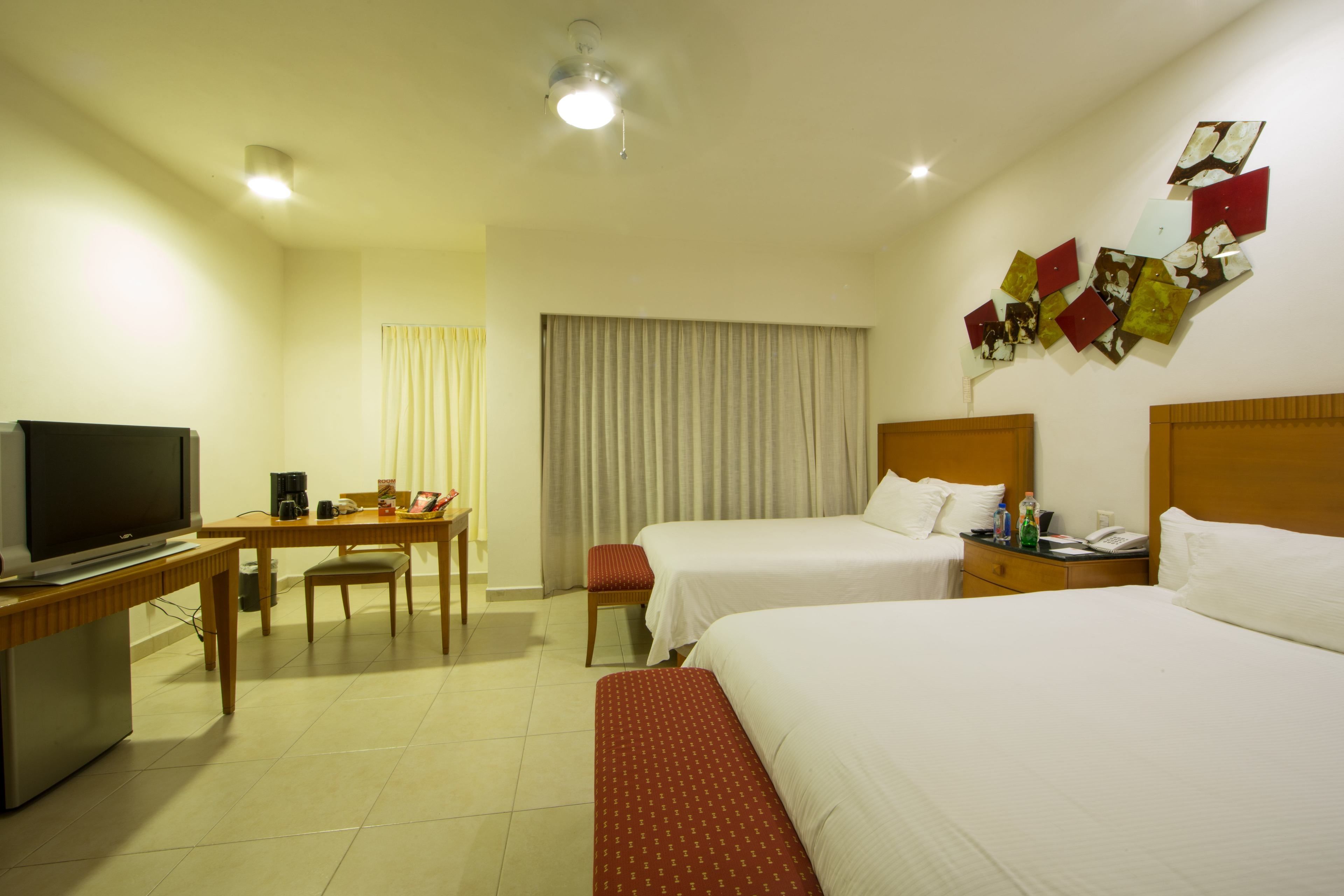 Quarto de hotel com duas camas, uma mesa de trabalho com televisão e uma obra de arte na parede.