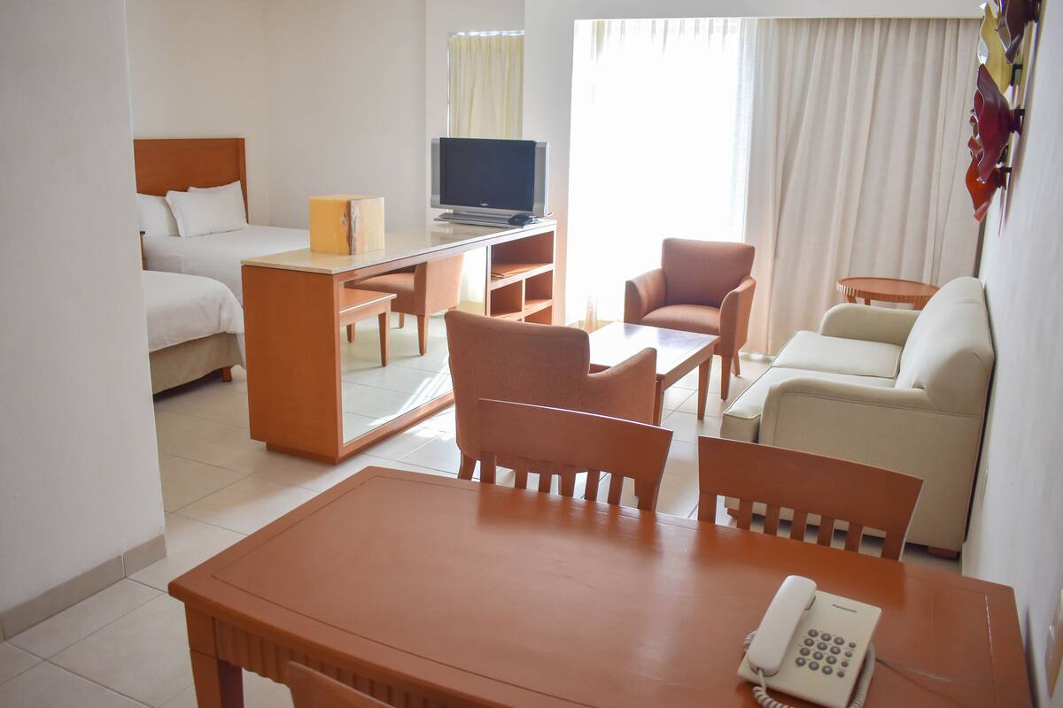 A hotel room with a bed, a desk with a television, a telephone, and two armchairs.