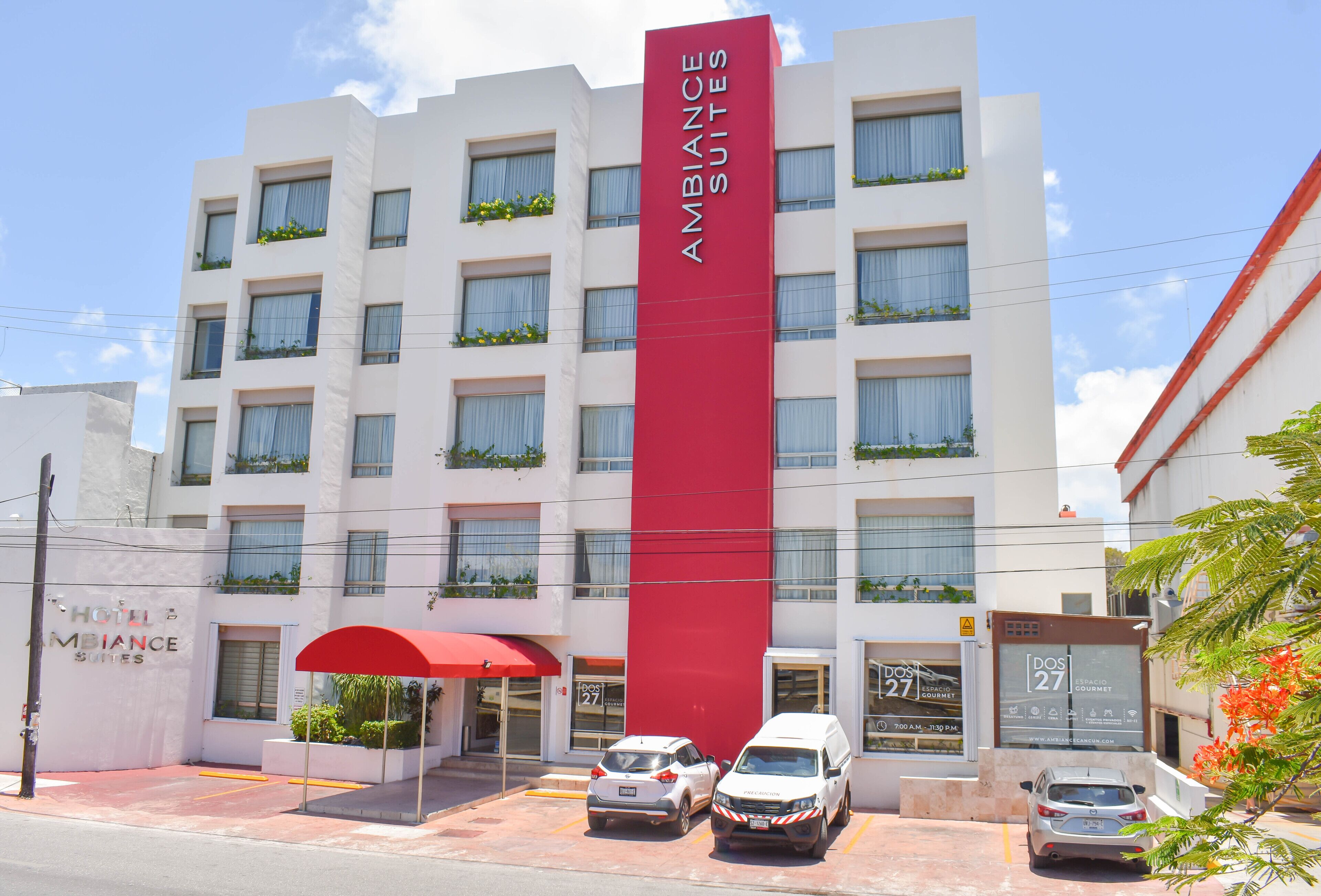 A hotel with a prominent red vertical sign, multiple balconies with plants, and a clear sky.