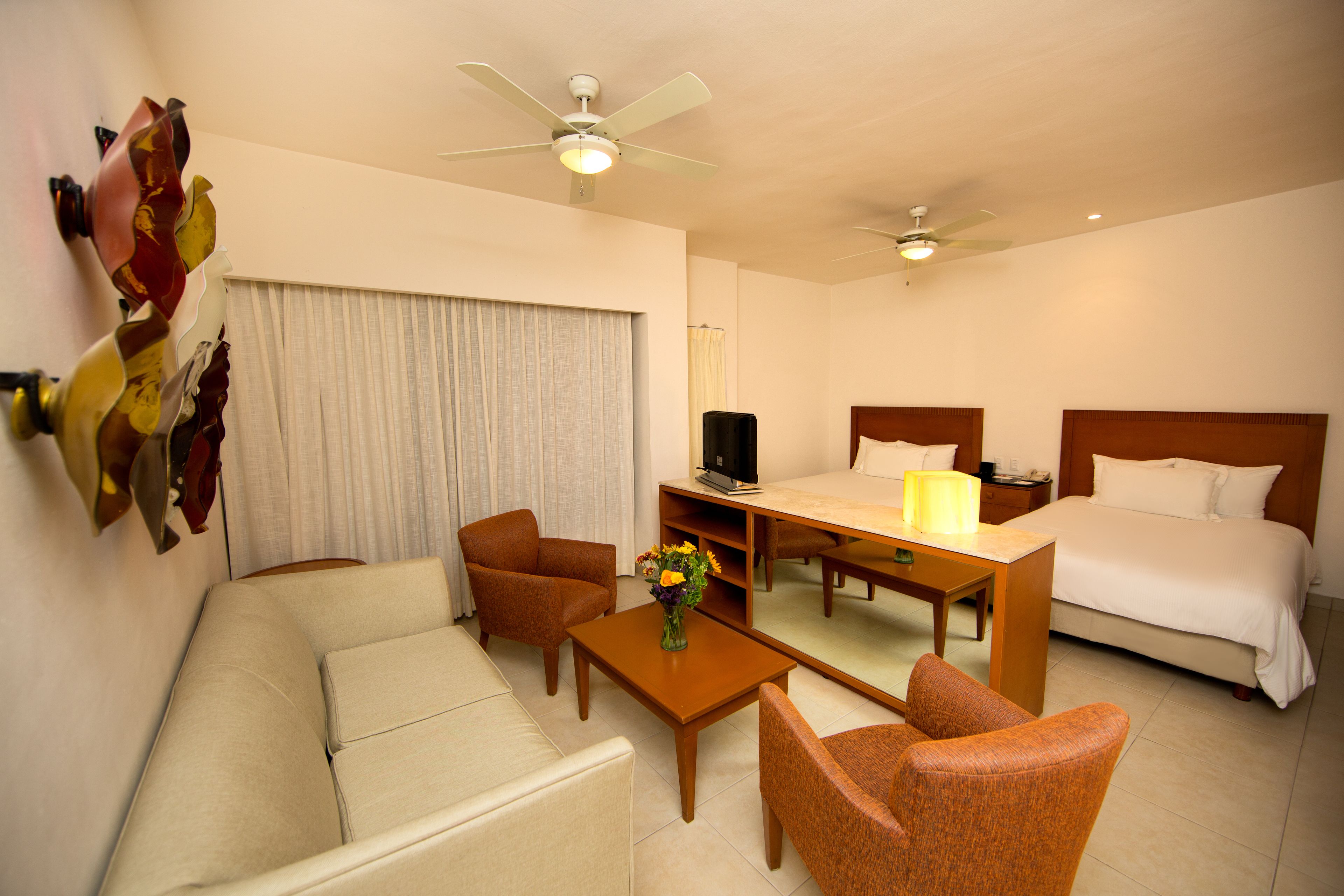 Une chambre d’hôtel comprenant un lit, un canapé, une chaise, une table basse, un téléviseur et un ventilateur de plafond.