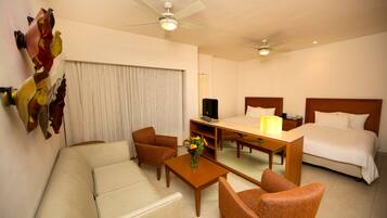 Une chambre d’hôtel comprenant un lit, un canapé, une chaise, une table basse, un téléviseur et un ventilateur de plafond.