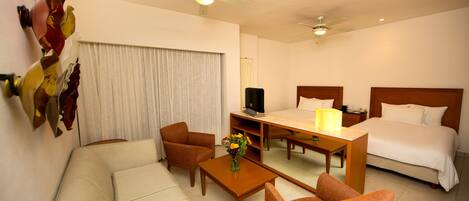 A hotel room with a bed, a sofa, a chair, a coffee table, a TV, and a ceiling fan.