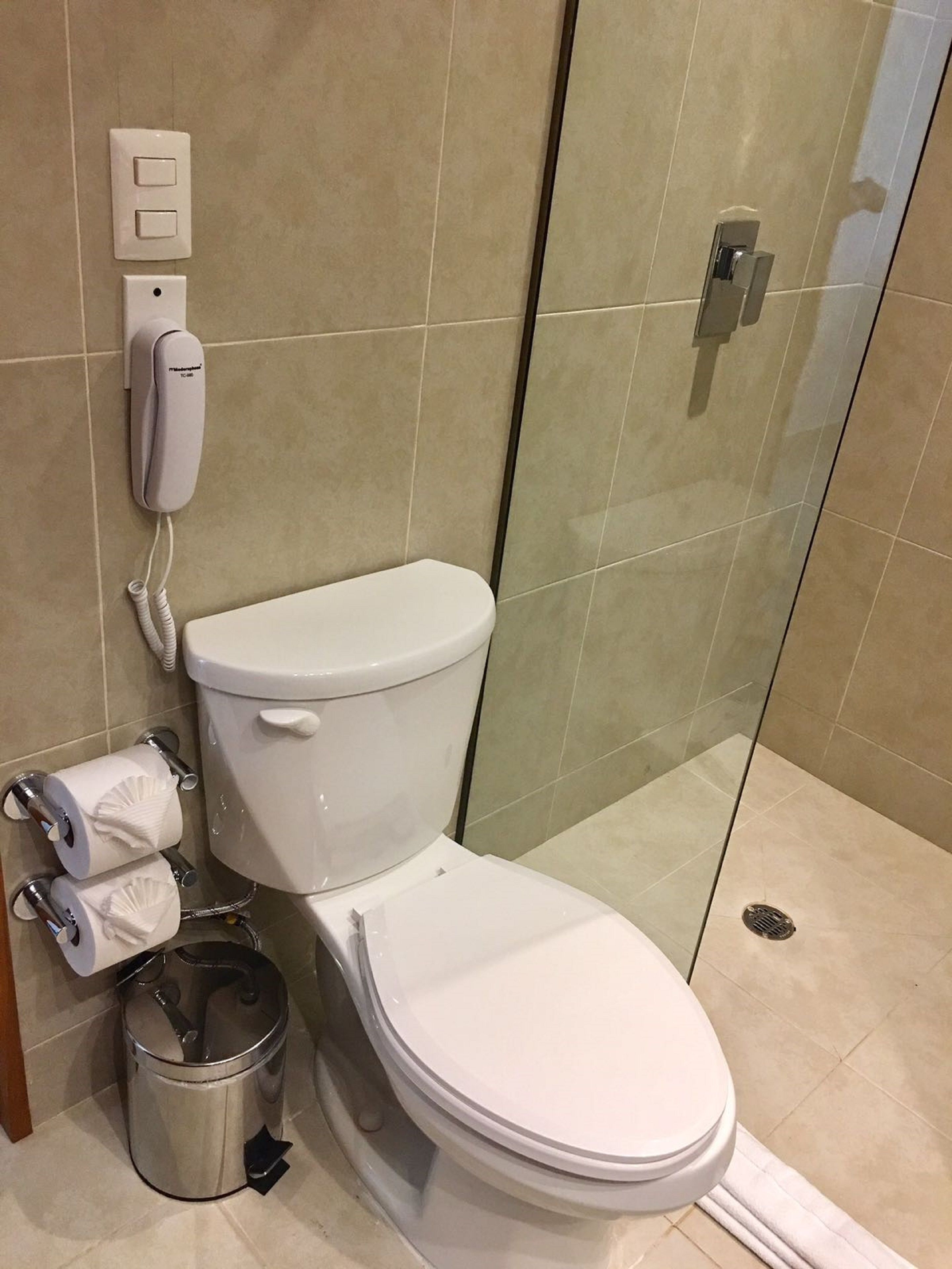 A modern bathroom with a toilet, a toilet paper holder, a trash can, and a glass shower enclosure.