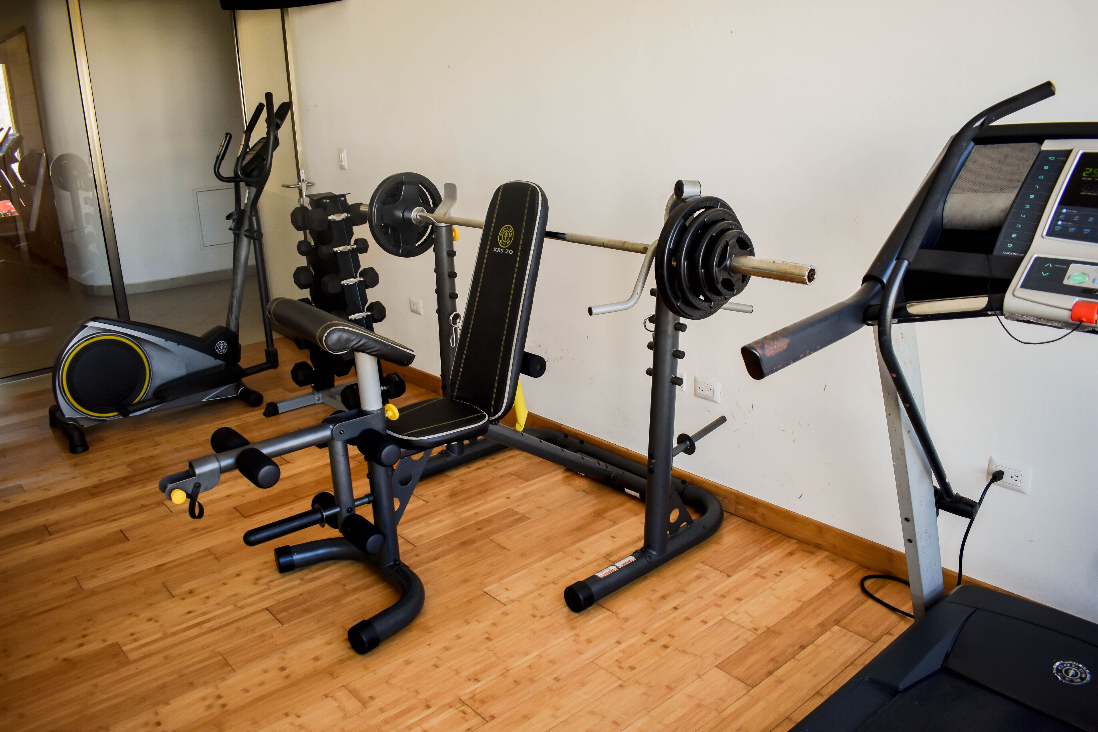 Uma academia em casa com supino, banco de musculação e esteira.