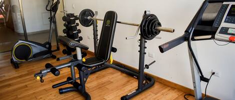 Uma academia em casa com supino, banco de musculação e esteira.