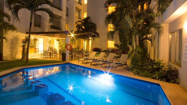 Una piscina con escalones de acceso, rodeada de palmeras y sillas de descanso.