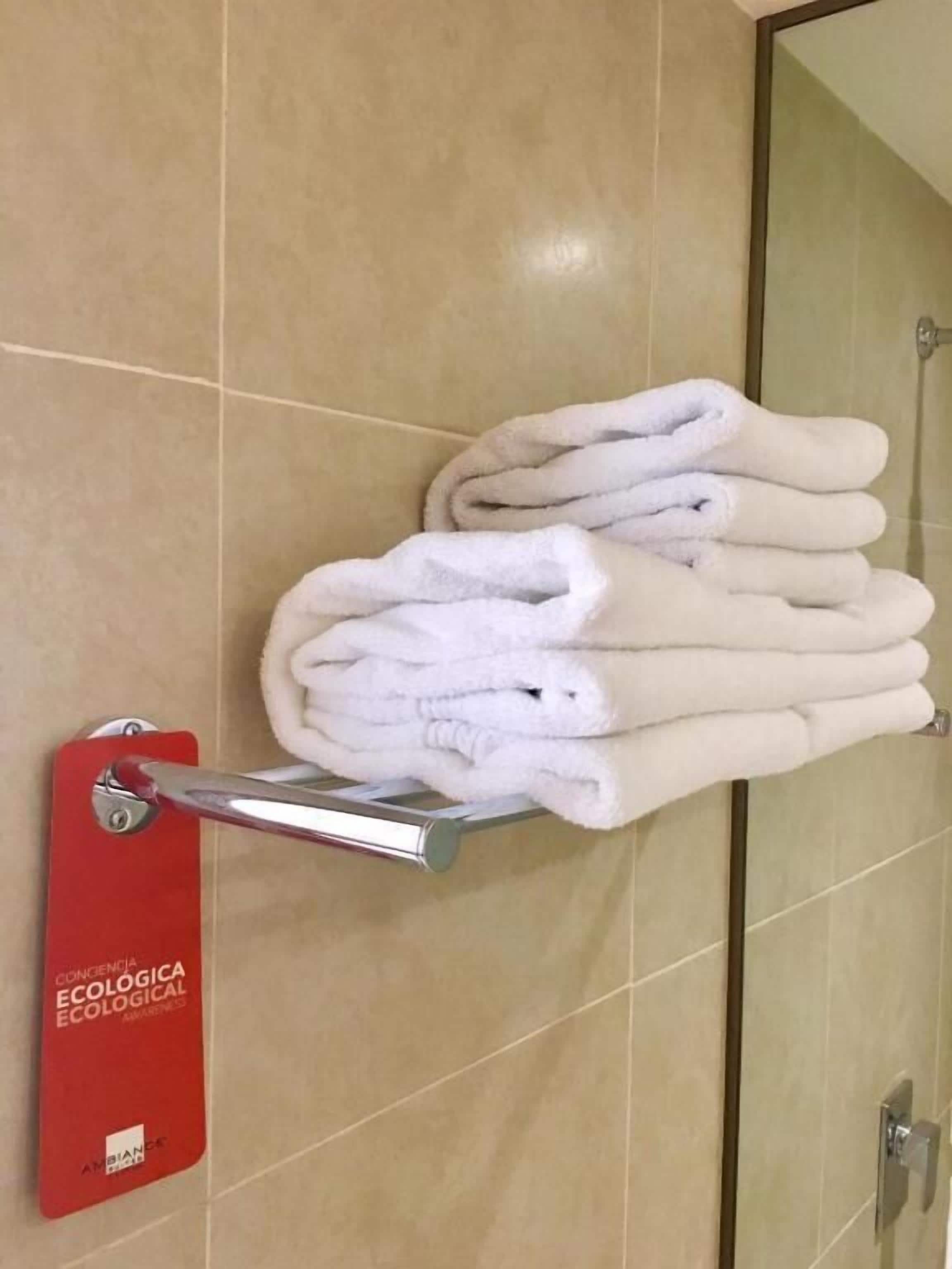 A stack of white towels on a metal towel rack in a bathroom with beige tiles.