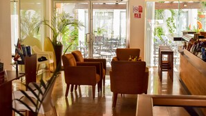 Un hall de hotel con mostrador de recepción, zona de estar y grandes ventanales con vistas a un jardín.