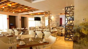 Un comedor moderno con sillas y mesas blancas, techo de madera y un panel decorativo en la pared.
