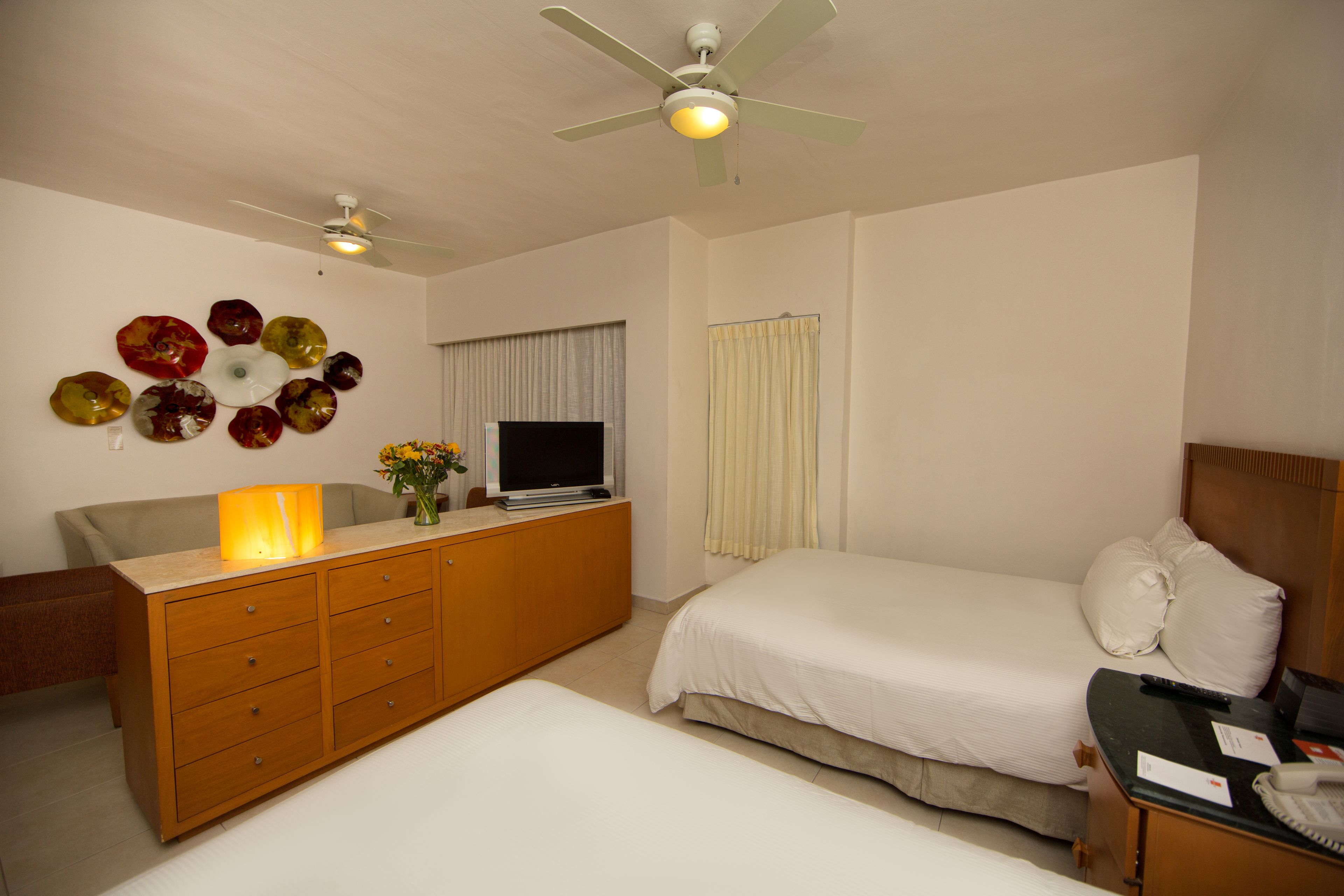 Un dormitorio con cama, cómoda, televisor y ventilador de techo.