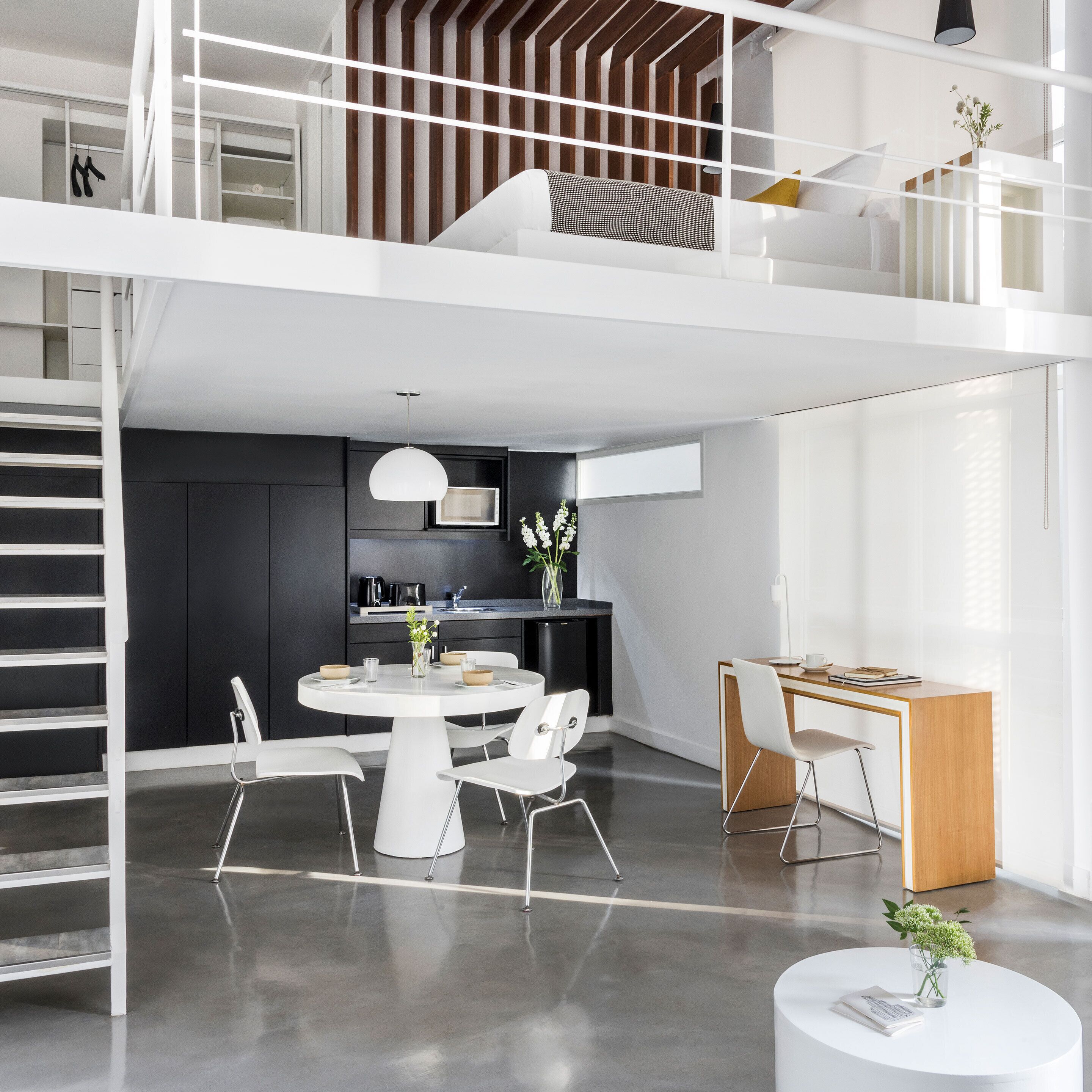Een modern loftappartement met een eethoek, keuken en een trap naar een verdieping.
