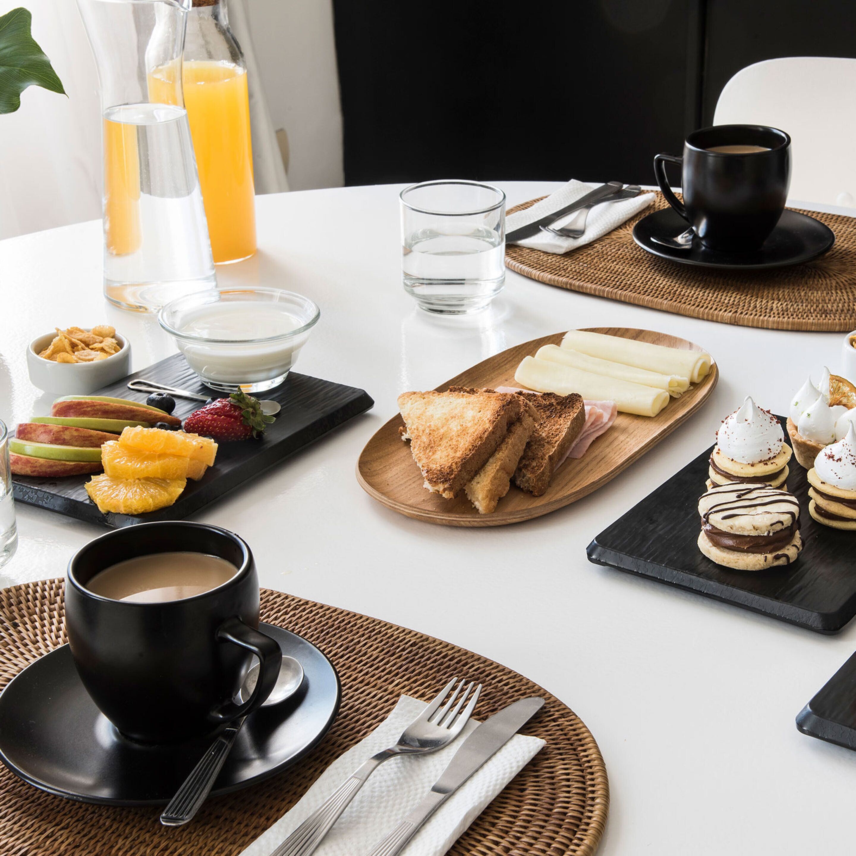 Una mesa con una variedad de alimentos para el desayuno, como tostadas, fruta y pasteles, además de bebidas y cubiertos.