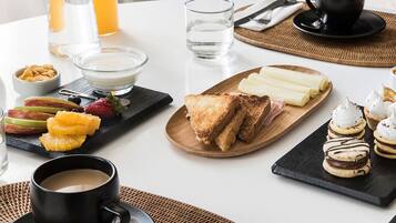 Una mesa con una variedad de alimentos para el desayuno, como tostadas, fruta y pasteles, además de bebidas y cubiertos.