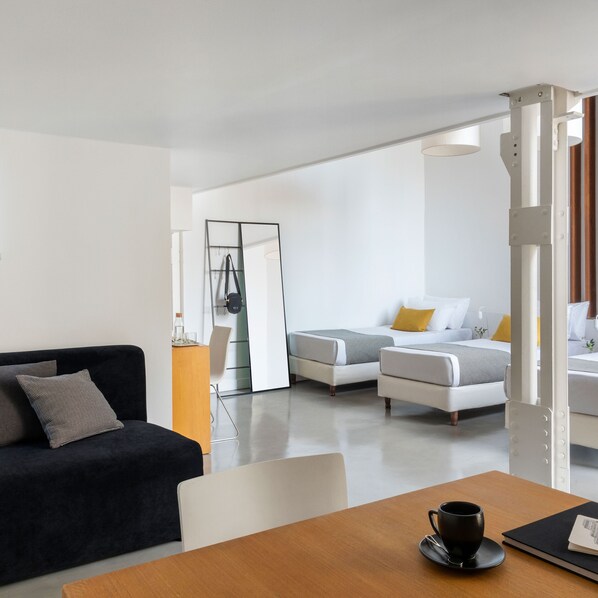 A modern hotel room with a sofa, two beds, a dining table, and a mirror. - HTL 9 de Julio Bs As (Buenos Aires)