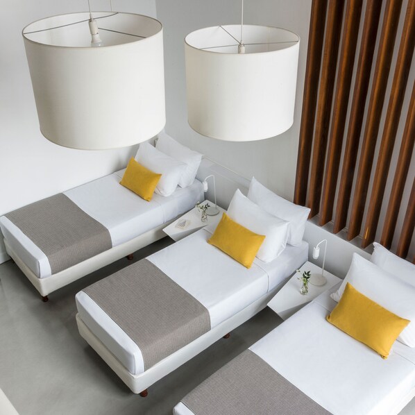 A hotel room with two single beds, each with a white mattress, a gray and white patterned bedspread, and a yellow pillow. There are two white pendant lamps hanging above the beds. - HTL 9 de Julio Bs As (Buenos Aires)