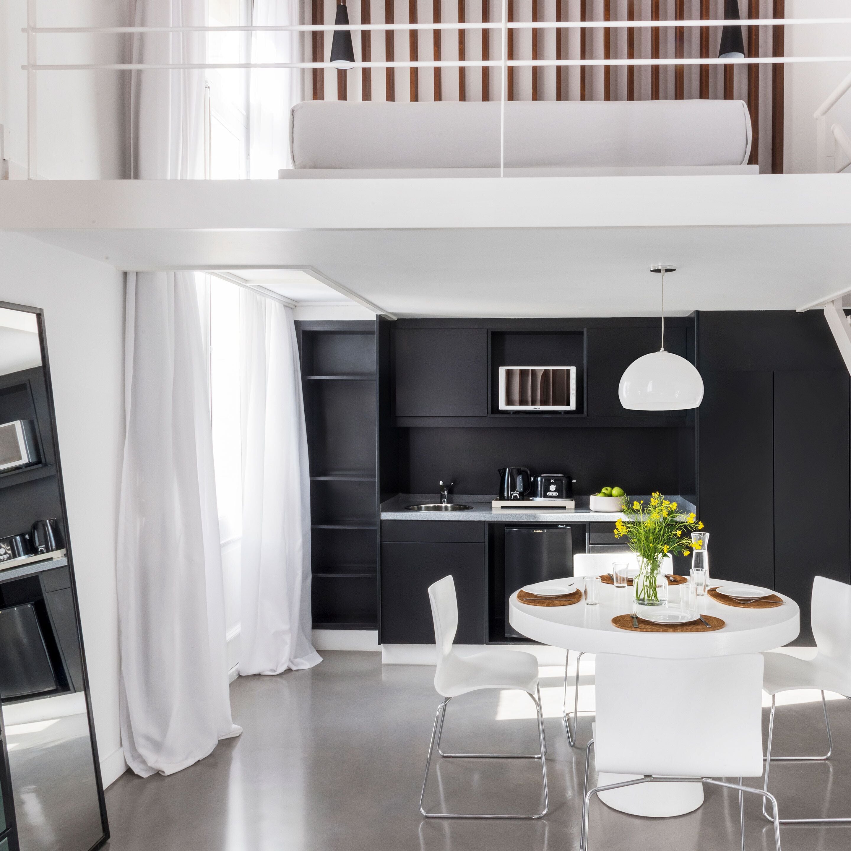 A modern kitchen with a dining area, featuring a round table, white chairs, and a black backsplash.