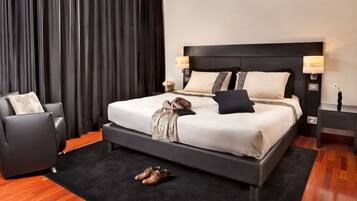 A modern hotel room with a large bed, a black headboard, two bedside lamps, a black rug, a wooden floor, and a black armchair.