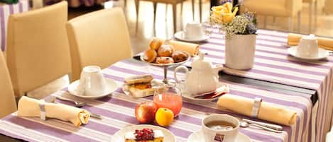 A dining table set with a variety of breakfast items including pastries, fruits, and beverages, arranged on a striped tablecloth.