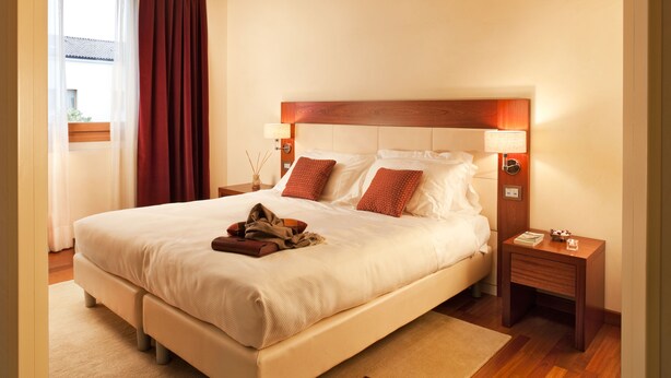 Habitación de hotel con una cama grande, cabecera de madera, mesitas de noche y vistas al exterior.