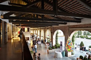 Un espacio interior amplio con techos altos y paredes de ladrillo a la vista. Varias mesas y sillas están dispuestas para comer o socializar.