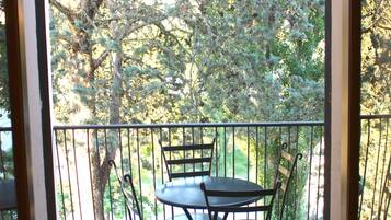 Un balcone con tavolo e sedie, una ringhiera e alberi sullo sfondo.