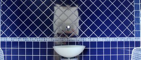 A bathroom with blue tiled walls, a white sink, and two blue patterned benches.