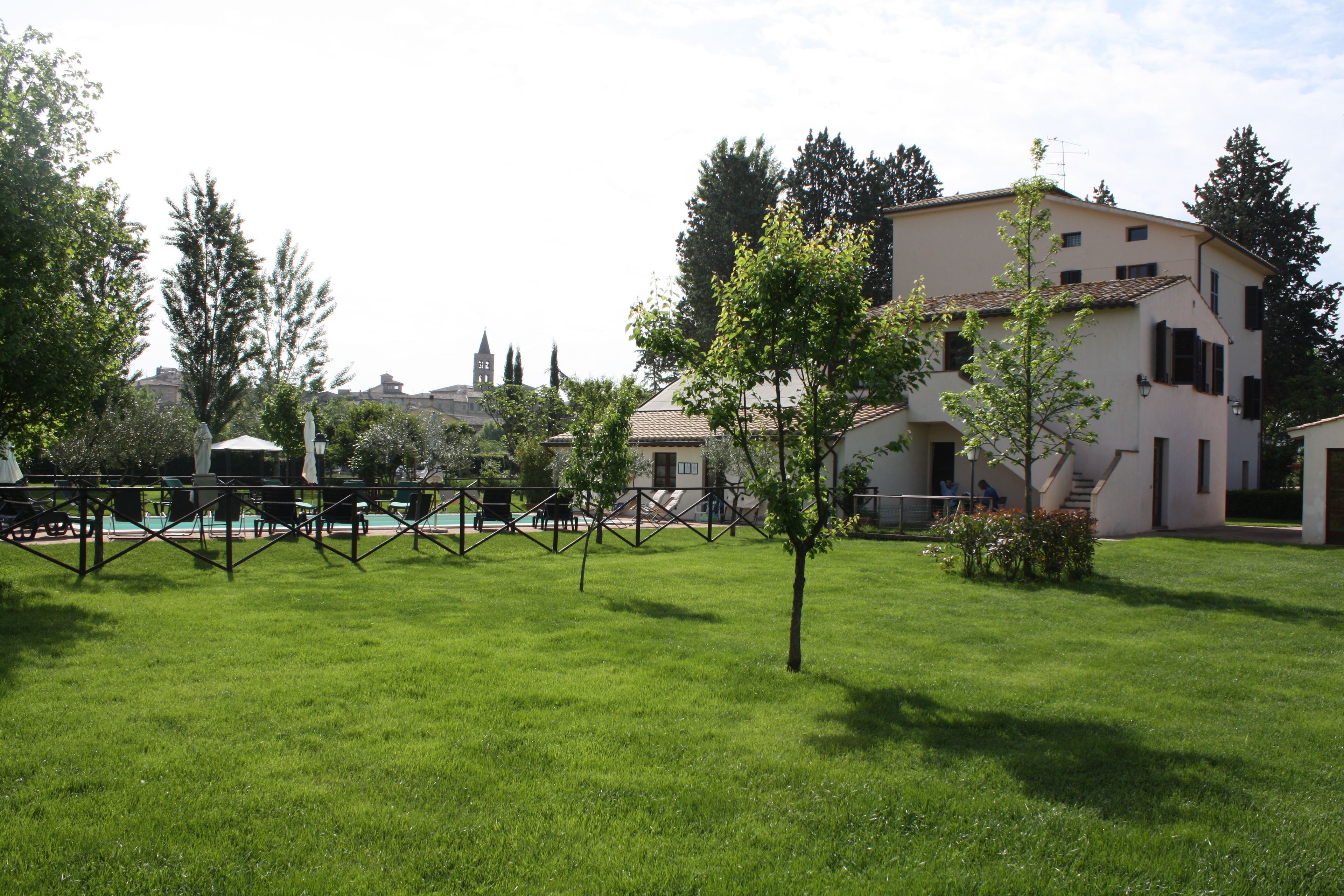 A grassy courtyard with a white building, a small tree, and a fence.
