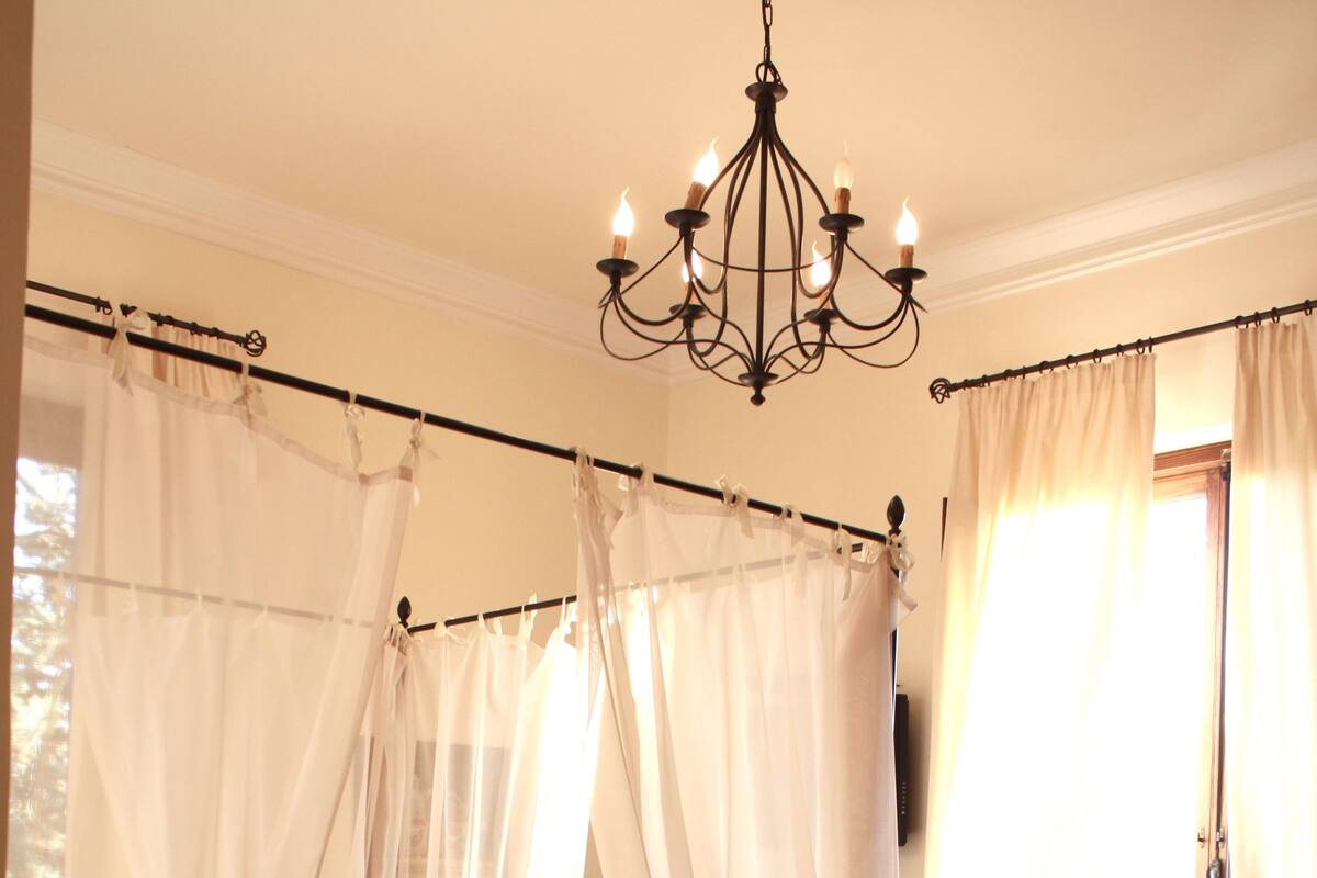 Une chambre à coucher avec un lit, une table de chevet avec une lampe, une fenêtre avec des rideaux et un radiateur.