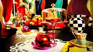 Una mesa con un calentador de tetera, tazas, un jarro a cuadros y un frutero.
