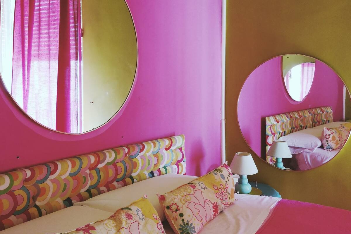 Una habitación con una cama, dos almohadas, una mesita de noche con lámpara y dos espejos redondos en las paredes.