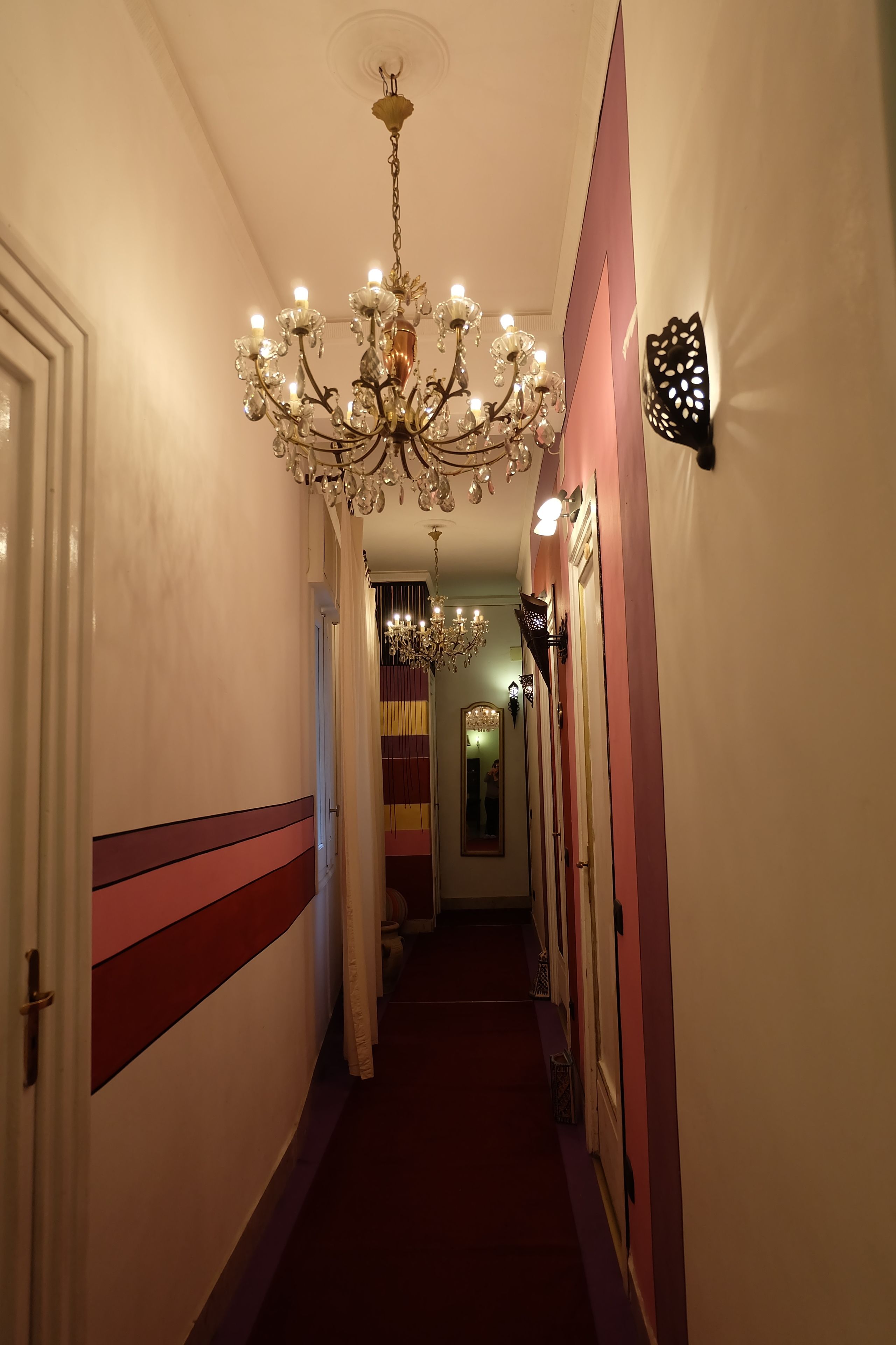 A hallway with a chandelier, striped walls, and a mirror.