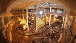 A multi-level atrium with a central circular seating area, multiple staircases, and hanging spherical light fixtures. - Esmeralda Praia Hotel (Natal)
