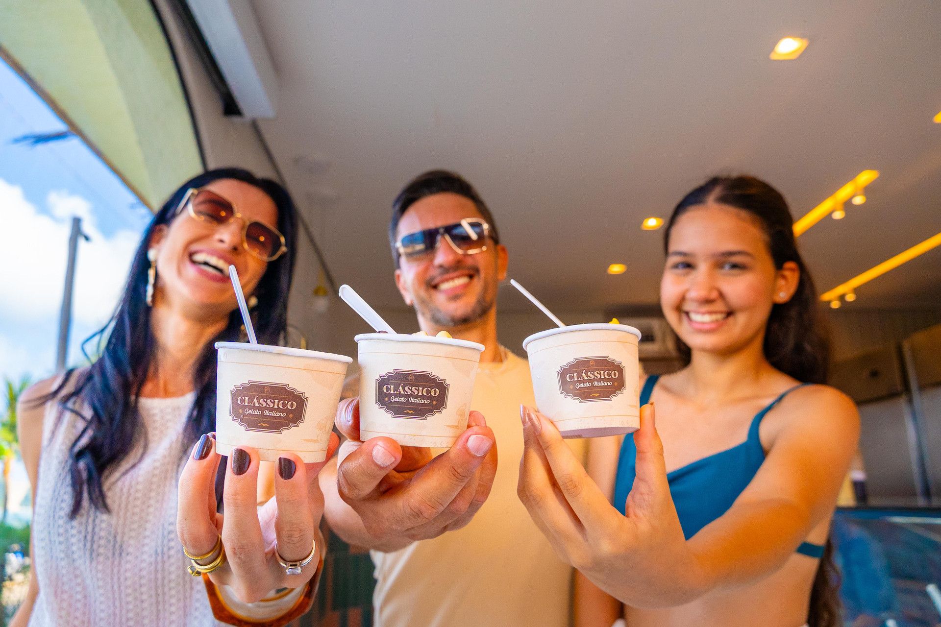 Três pessoas segurando copos de gelato da marca 'CLÁSSICO Gelato Italiano'.