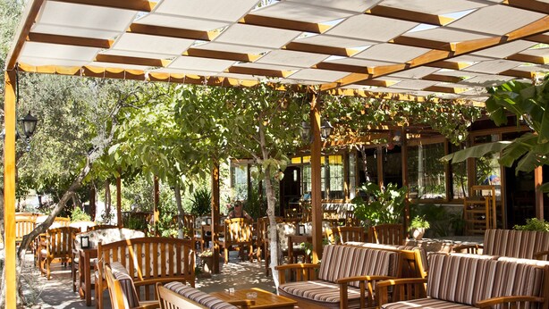 An outdoor seating area with wooden furniture and a pergola providing shade. - Gokcen Hotel & Apartments (Fethiye)