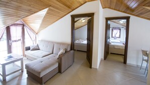 A spacious loft bedroom with a high ceiling, a large window with curtains, a sofa, a bedside table, and a chair. - Gokcen Hotel & Apartments (Fethiye)