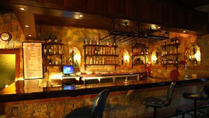 A bar with a stone wall, wooden ceiling, and bar stools. There is a menu board and a computer on the counter. - Gokcen Hotel & Apartments (Fethiye)