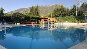 A swimming pool with a mountain backdrop, surrounded by lounge chairs and a bar area. - Gokcen Hotel & Apartments (Fethiye)