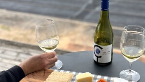 A table with a bottle of wine, two glasses, a plate of cheese, crackers, almonds, and dried fruit.