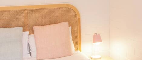 A neatly made bed with a pink blanket, white pillows, and a small bedside table with a lamp.