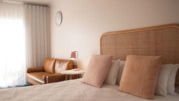 A hotel room with a bed, a brown leather sofa, a round table with a lamp, and a large window with curtains.