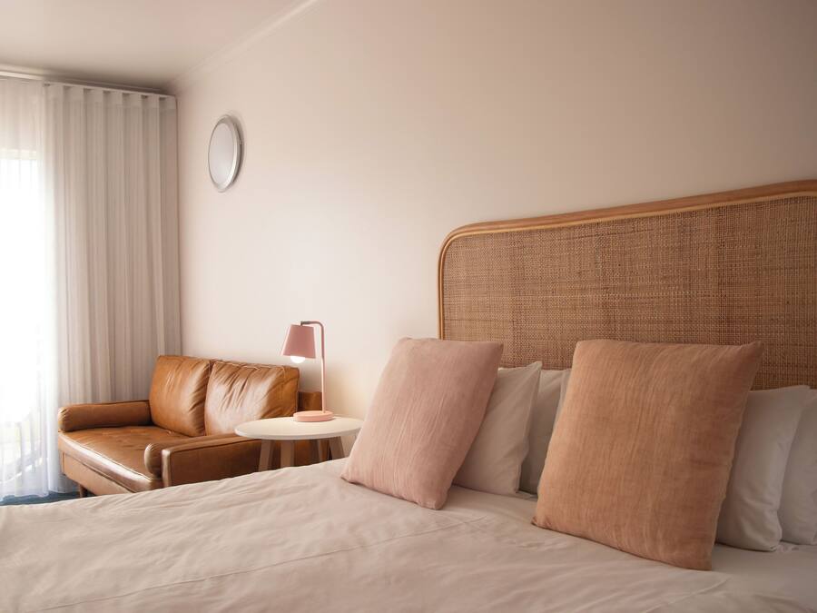 A hotel room with a bed, a brown leather sofa, a round table with a lamp, and a large window with curtains.