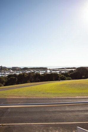 A coastal landscape with a grassy hill, a road, and a marina with boats. - Harbour View Motel (Robe)