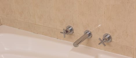 A bathtub with two faucets and a drain.
