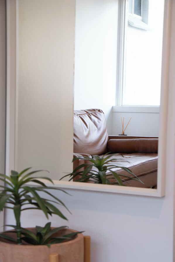 Una habitación con ventana, un sofá marrón, una mesita con difusor de aroma de junco y una planta en maceta.