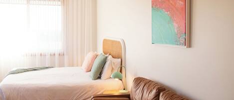 A bedroom with a bed, a nightstand, a lamp, a brown leather sofa, and a large abstract painting on the wall.